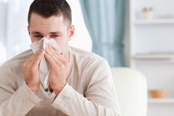 man sneezing due to poor indoor air quality and lack of air sealing at home in winter