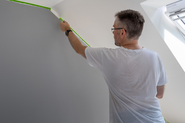 painter removes masking tape and creates a sharp border between colors on spray foam insulation painting