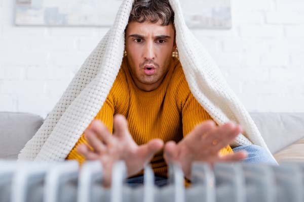 image of a homeowner in front of radiator depicting improper home insulation in winter