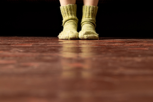 Women's legs in warm knitted socks on the floor depicting cold floor