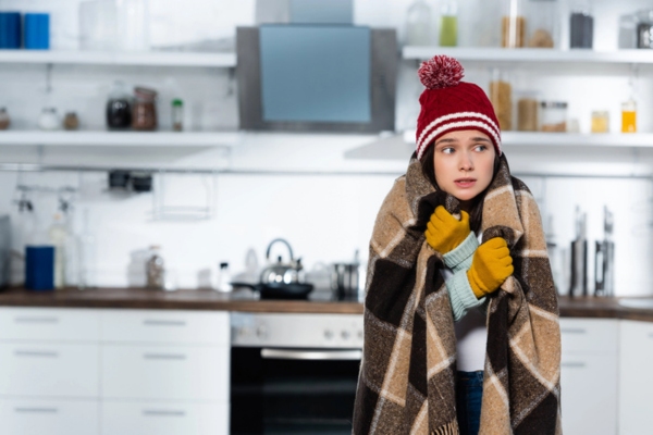 woman covered in blanket and full winter clothes while in the kitchen