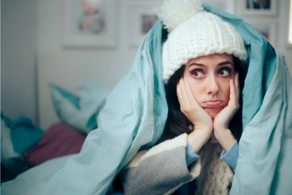 woman wrapped in blanket and in full winter gear due to feeling cold due to Older Homes Losing Energy