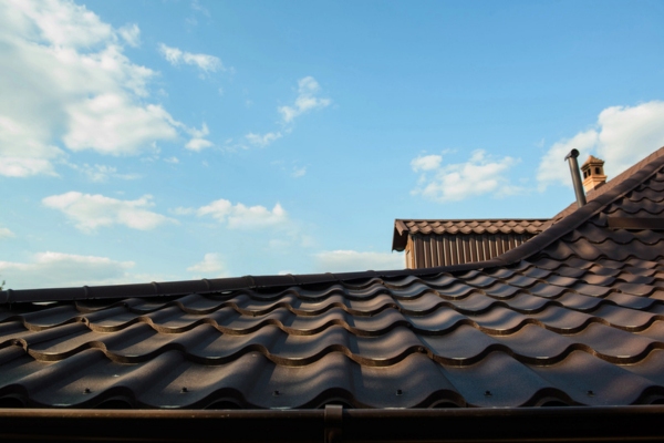 Brown roof of a house on a blue sky with clouds depicting heat transfer