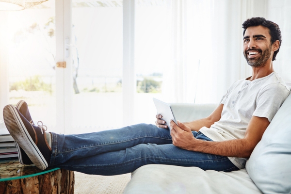 man lounging on a couch with his smart tablet depicting stable indoor temperature