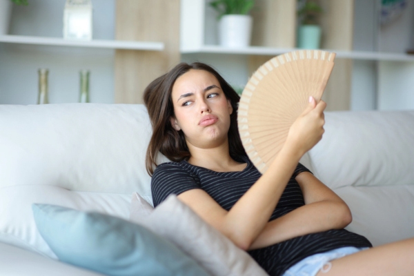 Overwhelmed woman using fan in a hot summer day while sitting on a couch