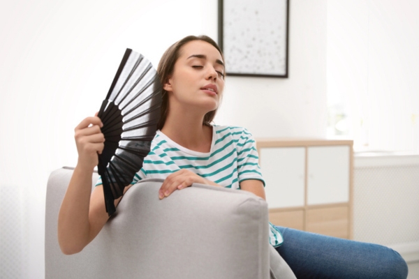 woman using hand fan indoors due to uneven temperature