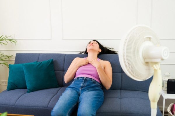 woman trying to keep cool in front of a stand fan depicting Air Conditioning Emergencies